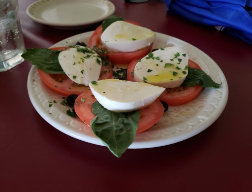 A plate of sliced tomatoes and mozzarella cheese, garnished with basil and olive oil.
