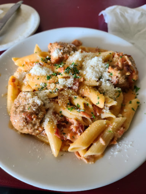 A plate of penne pasta topped with meatballs and grated cheese, garnished with parsley.