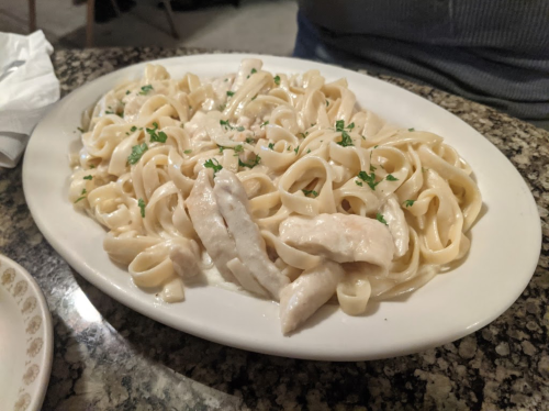 A plate of fettuccine alfredo with sliced chicken, garnished with parsley, on a marble table.