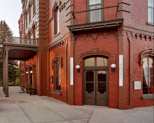 Historic red brick hotel entrance with large windows and decorative details, surrounded by trees.