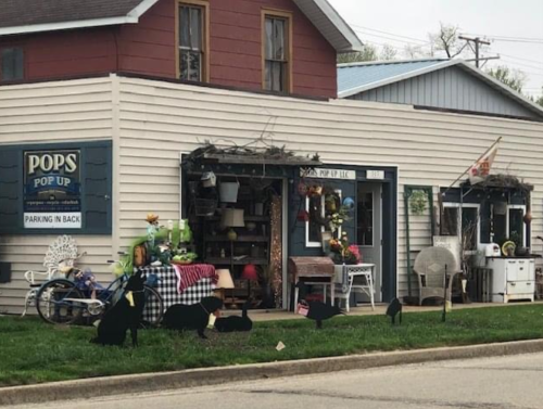 A quaint shop with a sign reading "Pops Pop Up," featuring outdoor decor and black silhouettes of animals in front.