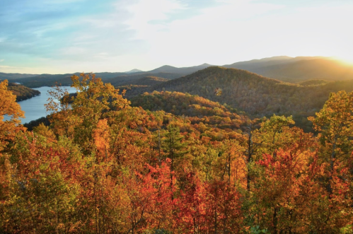 A scenic view of mountains and a lake surrounded by vibrant autumn foliage at sunset.