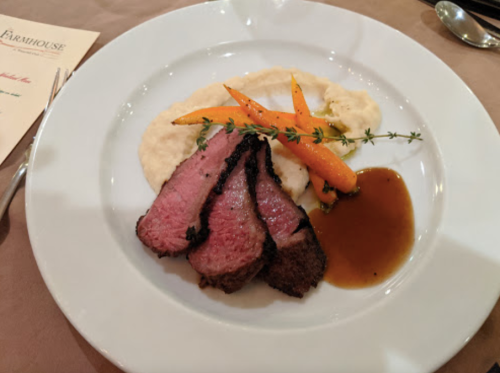 A plate of sliced beef with a side of creamy mashed potatoes, glazed carrots, and a drizzle of sauce.