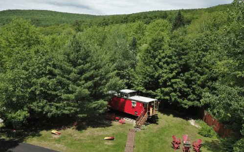 A red train car converted into a cabin, surrounded by lush green trees and a grassy area.