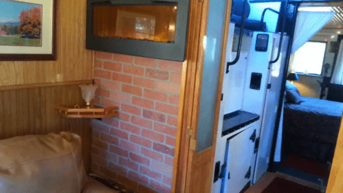 Cozy interior view of a cabin with a brick wall, a small couch, and a glimpse of a bedroom in the background.