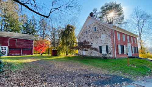 Historic red and stone house with a barn, surrounded by trees and colorful autumn foliage under a clear blue sky.
