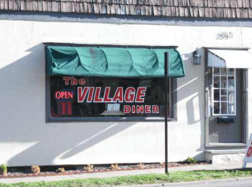 A diner window with a green awning displays a bright "OPEN" sign and the name "The Village Diner."