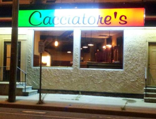 A brightly lit restaurant exterior at night, featuring a colorful sign that reads "Cacciatore's."