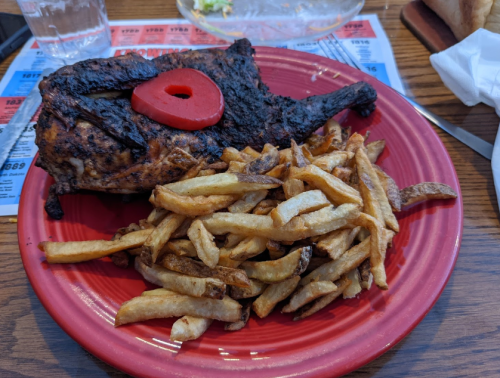 A plate with a grilled chicken leg topped with a slice of tomato, served alongside a generous portion of French fries.