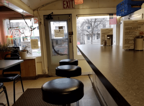 Interior of a diner with a counter, black stools, and a door leading outside, featuring American flags and menus.