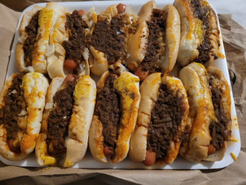 A tray of hot dogs topped with seasoned beef, onions, and mustard, arranged in a neat row.