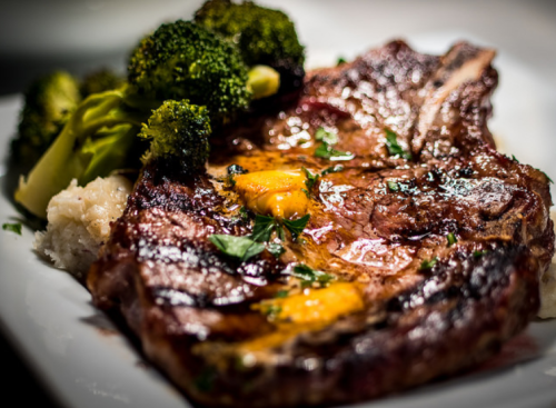 A juicy grilled steak topped with egg yolk, served with broccoli and mashed potatoes on a white plate.
