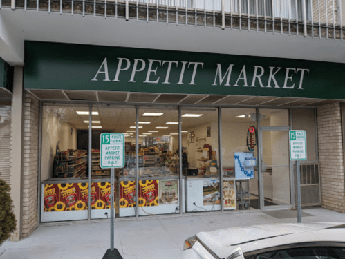 Exterior of Appetit Market with large windows displaying products and parking signs in front.