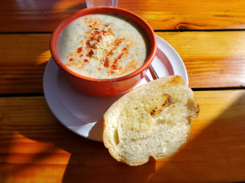 A bowl of creamy soup topped with spices, served with a slice of toasted bread on a wooden table.