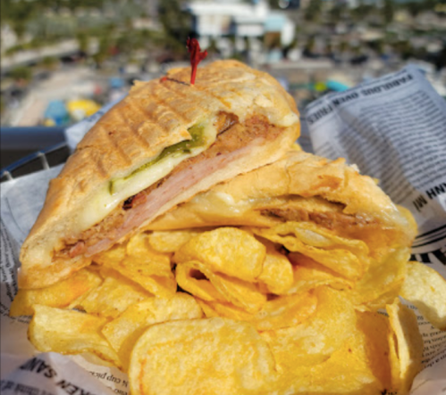 A close-up of a toasted sandwich with layers of meat and cheese, served with a side of potato chips.