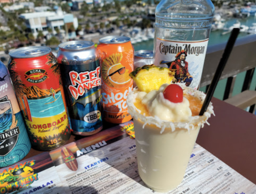 A tropical cocktail with a cherry and pineapple, surrounded by colorful beverage cans and a bottle of Captain Morgan.