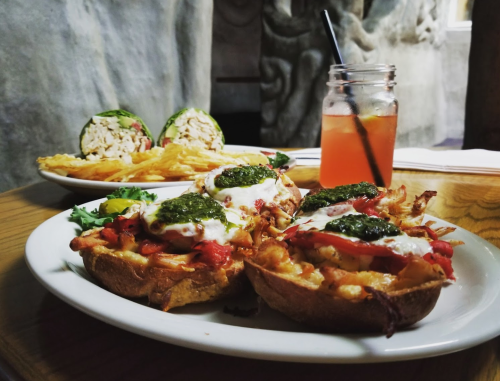 A plate with two loaded potato skins topped with cheese and sauce, alongside a sandwich, fries, and a drink.