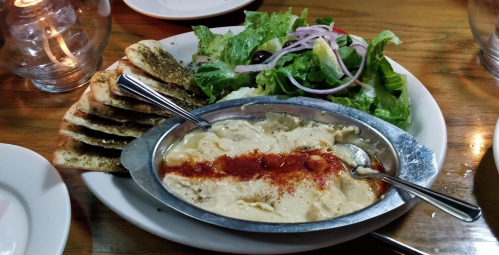 A plate of hummus drizzled with olive oil and spices, served with pita bread and a fresh salad on the side.