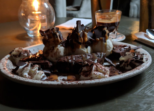 A plate of decadent chocolate dessert topped with whipped cream, chocolate drizzle, and a glass of coffee in the background.