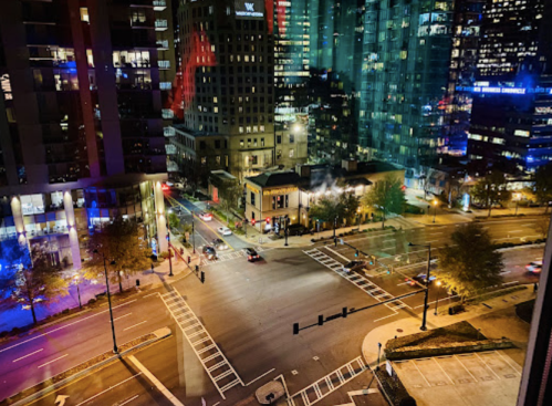 Aerial view of a city intersection at night, illuminated buildings, and streetlights creating a vibrant urban scene.