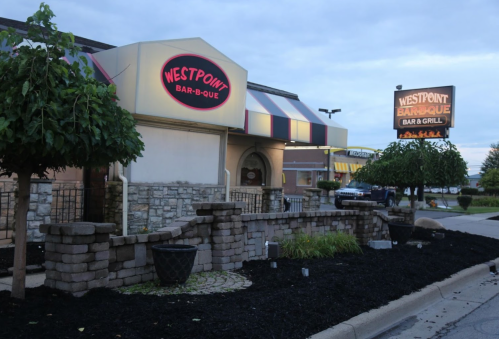 Exterior view of Westpoint Bar-B-Que restaurant, featuring a sign and landscaped area with trees and stonework.