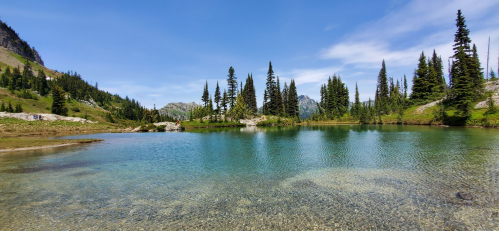 A serene lake surrounded by lush green trees and mountains under a clear blue sky.