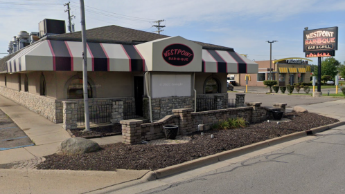 Exterior view of Westpoint Bar-B-Que Bar & Grill, featuring a striped awning and stone facade, with nearby signage.