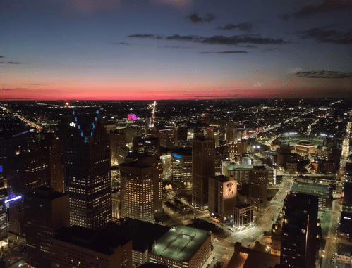 Aerial view of a city skyline at dusk, with lights twinkling and a colorful sunset in the background.