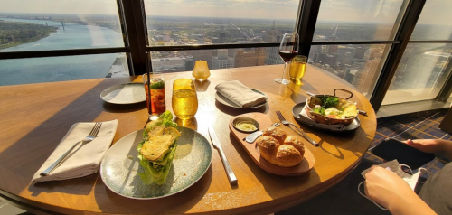 A table set with gourmet dishes, drinks, and a view of the city skyline through large windows.