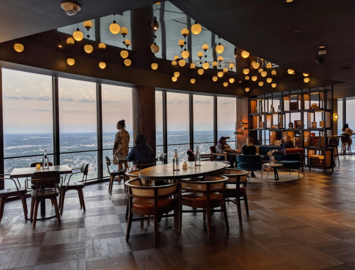 A modern restaurant with large windows, stylish decor, and patrons enjoying the view and ambiance.