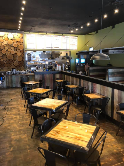 Interior of a restaurant featuring wooden decor, metal tables, and a visible kitchen area in the background.