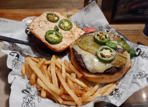 A burger with jalapeños and melted cheese on a bun, served with a side of crispy fries on a paper-lined plate.