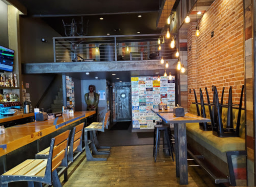 Interior of a rustic restaurant with wooden bar, stacked chairs, and a wall of license plates. Warm lighting enhances the ambiance.