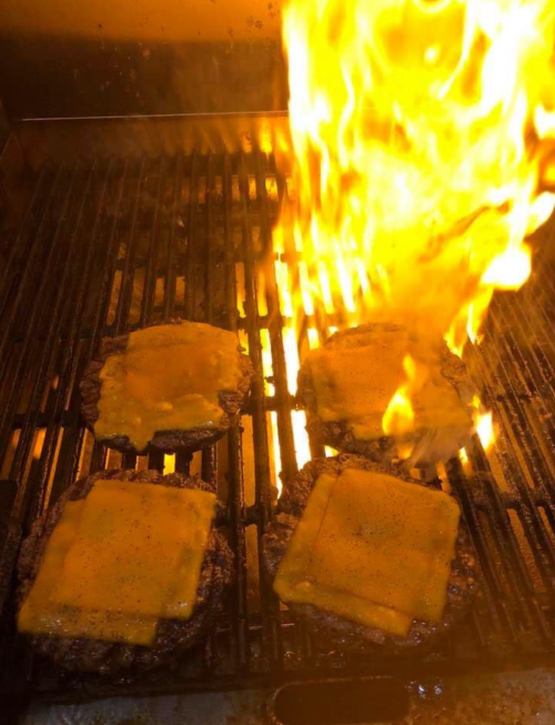 Grilling burgers with melted cheese, flames rising from the grill.