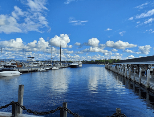 A serene marina with boats docked, under a bright blue sky filled with fluffy clouds.