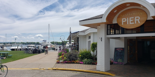 A scenic view of Stafford's Pier with boats, a bike path, and colorful flowers along the waterfront.