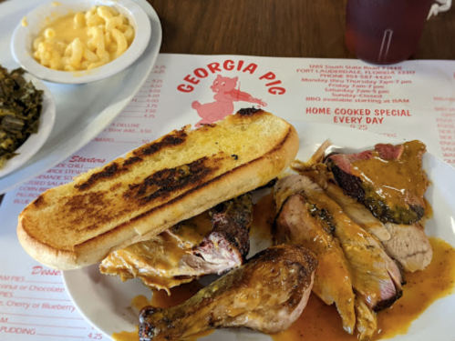 A plate of BBQ chicken with sauce, toasted bread, and sides of macaroni and greens, on a restaurant menu backdrop.