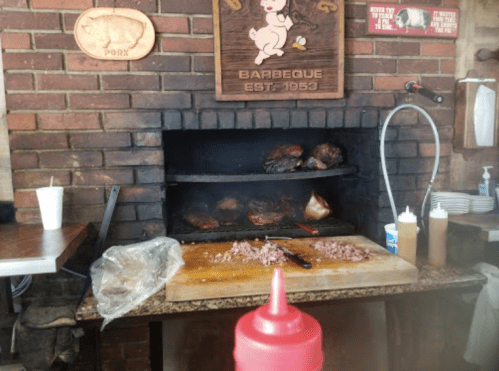 A barbecue pit with smoked meats, a cutting board with chopped meat, and condiments on a table in a rustic setting.