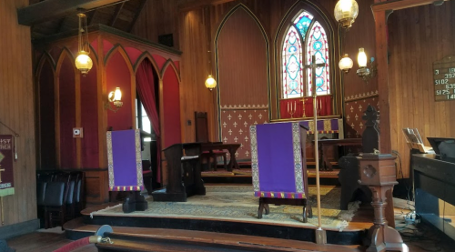 Interior of a church featuring stained glass windows, wooden walls, and purple altar cloths.