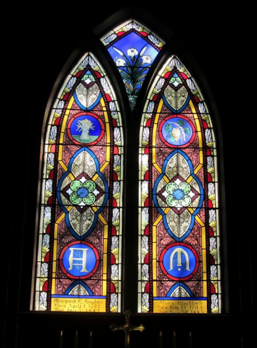 Stained glass window featuring intricate designs and vibrant colors, with symbols and floral motifs.