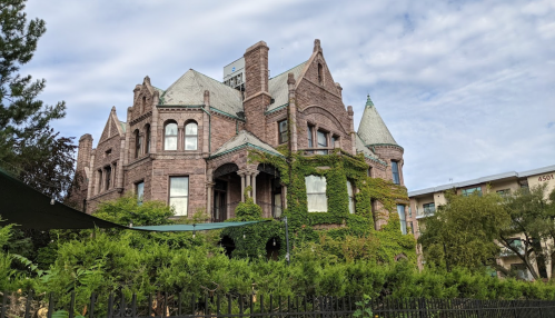 A large, historic stone mansion covered in greenery, featuring turrets and intricate architectural details.