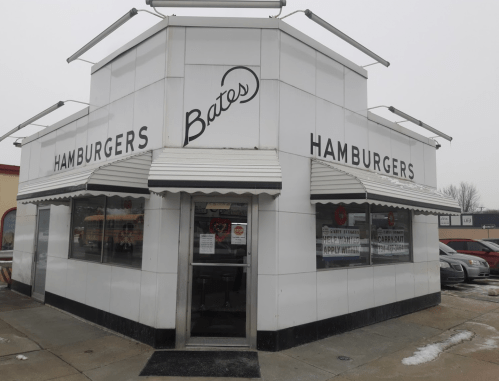 A white, retro-style hamburger restaurant with large "Bates Hamburgers" signage and awnings, set in a snowy environment.