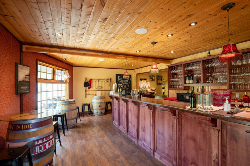 A cozy bar with wooden decor, wine barrels, and a well-stocked counter, featuring warm lighting and a welcoming atmosphere.