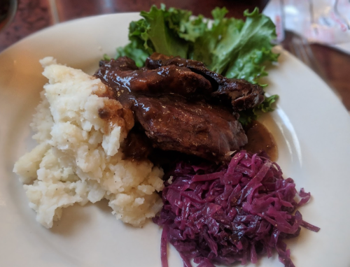 A plate featuring mashed potatoes, beef with gravy, and purple cabbage, garnished with lettuce.
