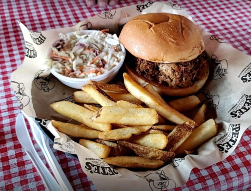 A plate with a pulled pork sandwich, coleslaw, and crispy fries on a checkered tablecloth.