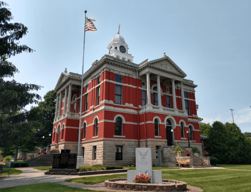 Historic red brick courthouse with a clock tower, American flag, and landscaped grounds on a clear day.