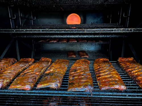 Smoked ribs on a grill, with a glowing firebox in the background, showcasing a rich, smoky flavor.