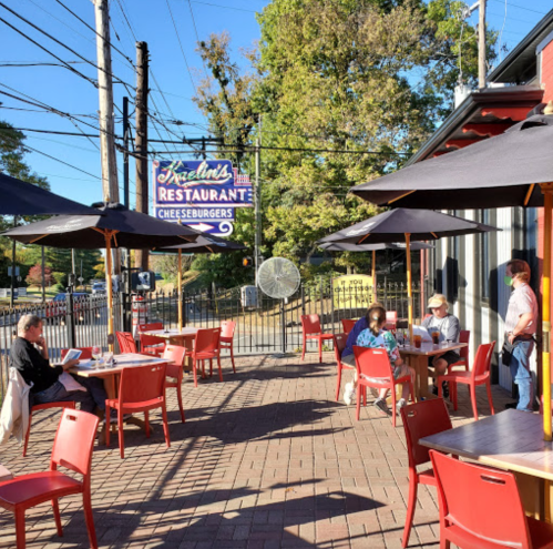 Outdoor dining area at a restaurant with tables, umbrellas, and a sign for "Izell's Restaurant" in the background.