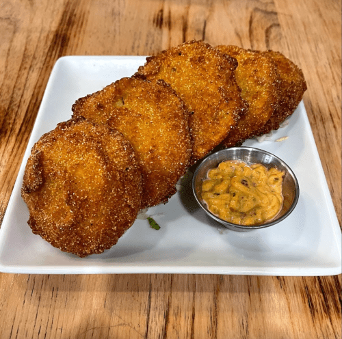 Four golden-brown fritters on a plate, served with a small bowl of dipping sauce.