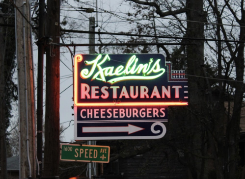 Neon sign for Kaelin's Restaurant, featuring "Cheeseburgers" and an arrow, set against a dusk sky.